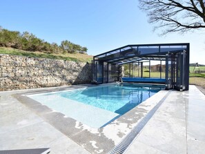 Ein Schwimmbecken mit Steinmauer und einer gläsernen Sitzgruppe.