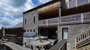 A two-story stone building with a wooden deck, outdoor seating, and a hot tub. - Luxurious Villa in Nadrin Belgium with Sauna & Hot Tub (Houffalize)