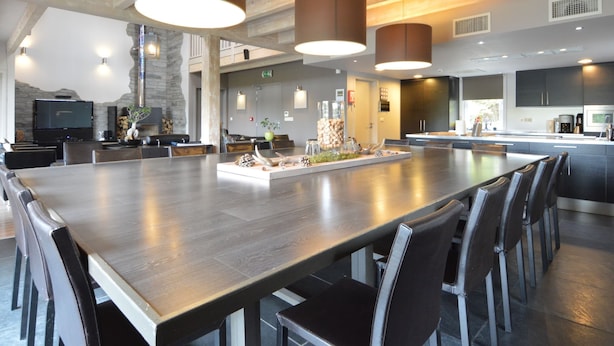 A modern dining area with a large table, multiple chairs, pendant lighting, and a stone accent wall. - Luxurious Villa in Nadrin Belgium with Sauna & Hot Tub (Houffalize)
