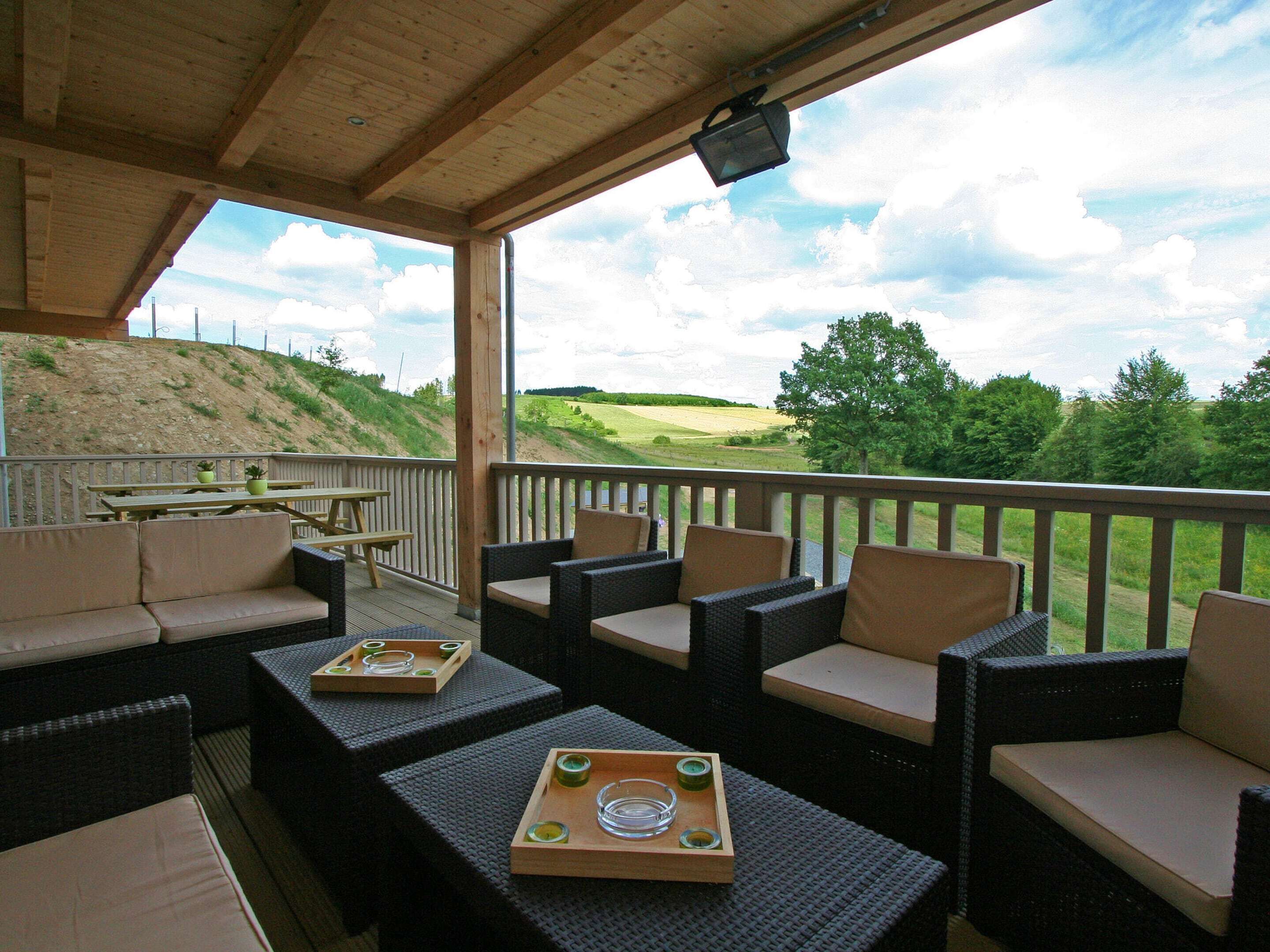 Een overdekt terras met rieten meubels en een houten tafel, met uitzicht op een golfbaan.