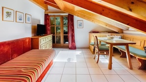 Um quarto de sótão acolhedor com teto de madeira, sofá, televisão, mesa de jantar e cozinha.