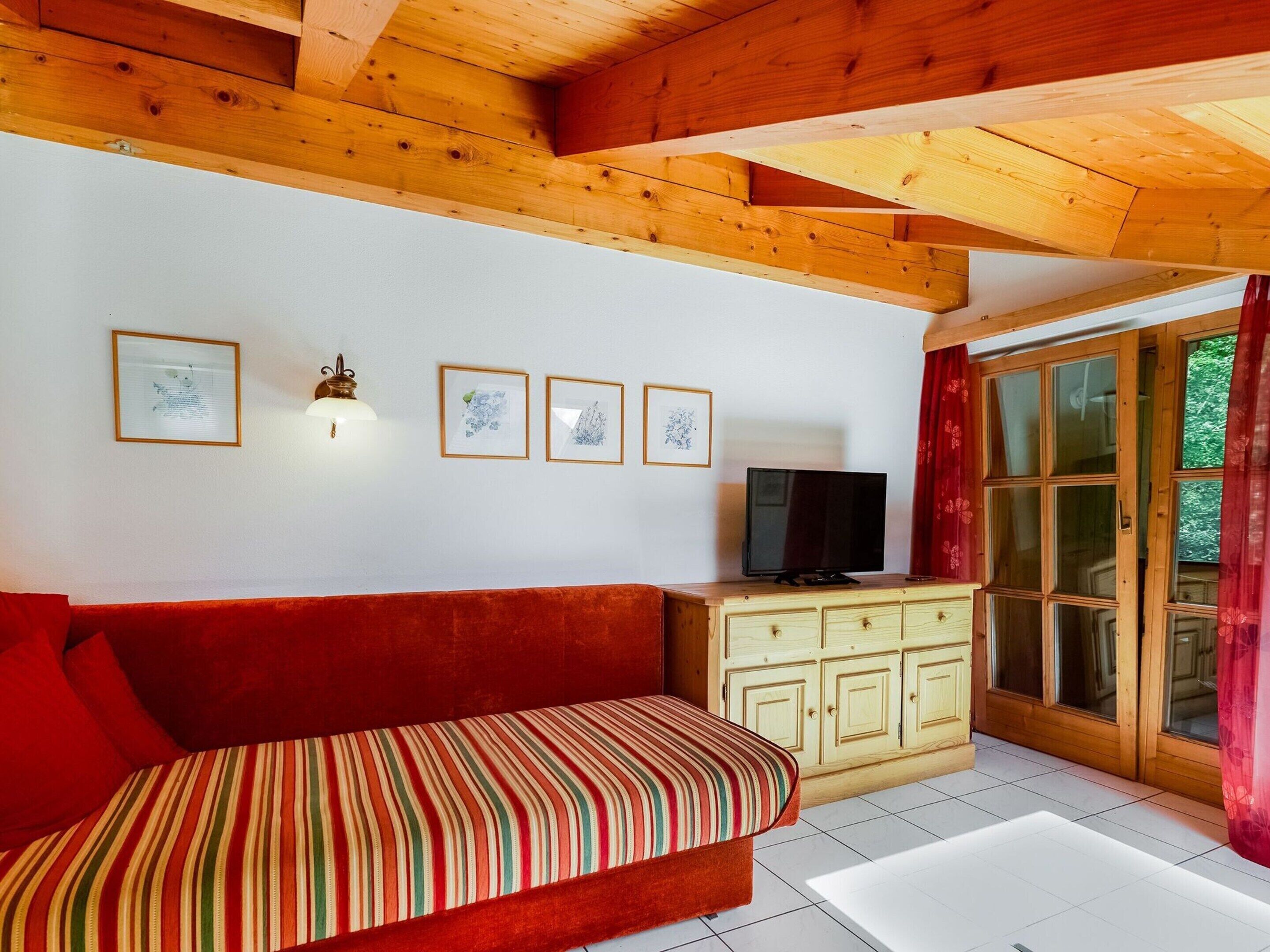 Una habitación acogedora con techo de madera, un sofá rojo, un televisor y un armario.