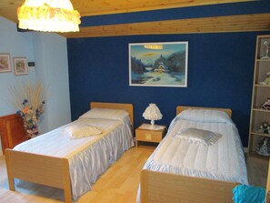 Un dormitorio con dos camas de madera, una mesita de noche con una lámpara, un cuadro en la pared y un florero con flores secas.