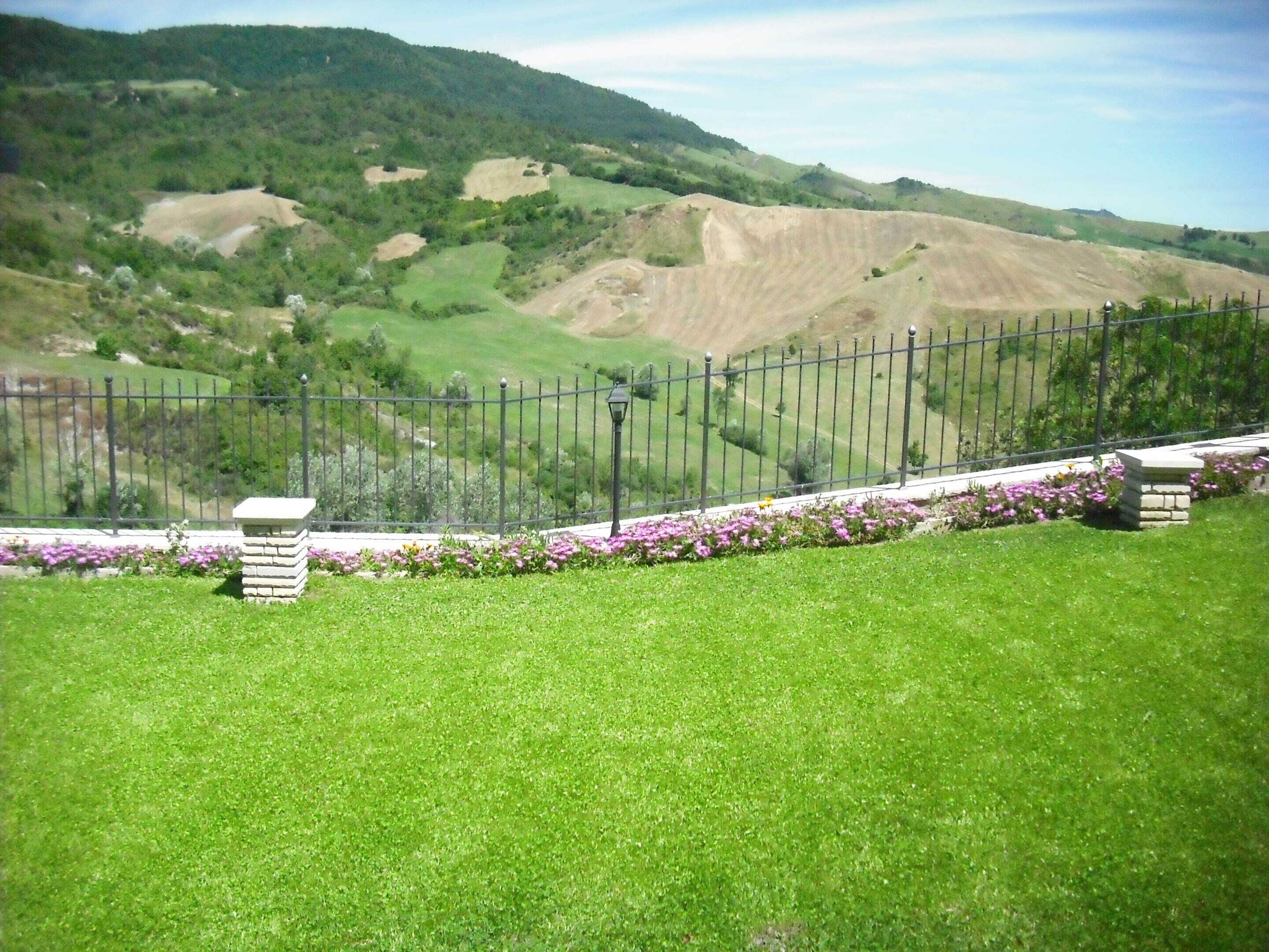 A grassy area with a metal fence and a stone structure.