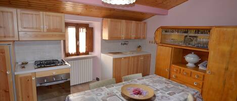 A kitchen with wooden cabinets, a gas stove, a dining table with chairs, and a chandelier.