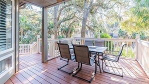 A covered outdoor deck with a table and chairs, surrounded by trees. - 4 Lark Street - 4th Row North Forest Beach (Hilton Head Island)