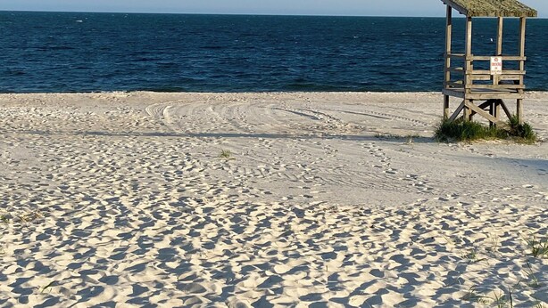 Ein sandiger Strand mit einem hölzernen Rettungsturm und dem Ozean im Hintergrund.