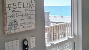 Eine Wandtafel mit der Aufschrift 'FEELIN' beachy Gulf Shores Alabama' und Blick auf einen Strand durch ein Fenster.