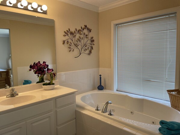 A bathroom with a large mirror, a vanity with a sink, a bathtub, and a window with blinds.
