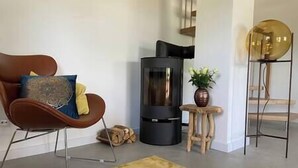Un salon moderne avec un canapé en cuir marron, un poêle à bois noir, une petite table en bois sur laquelle est posée une plante, et un grand objet sphérique doré placé sur un socle.