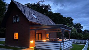 Une maison en briques avec un patio couvert, une fenêtre bien visible et une clôture blanche en bois.