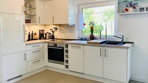 Une cuisine moderne avec des meubles blancs, un four encastré et une fenêtre donnant sur un paysage verdoyant.