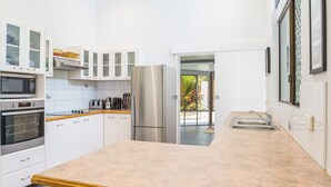 A modern kitchen with white cabinetry, a stainless steel refrigerator, and a large island with stools. - Tropical Beachside Home - Pool, Wifi (Holloways Beach)