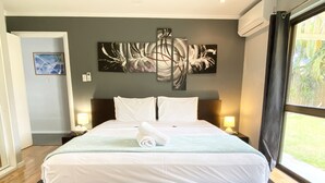A large bed with white linens, two bedside lamps, and a view of the outdoors through a window. - Tropical Beachside Home - Pool, Wifi (Holloways Beach)