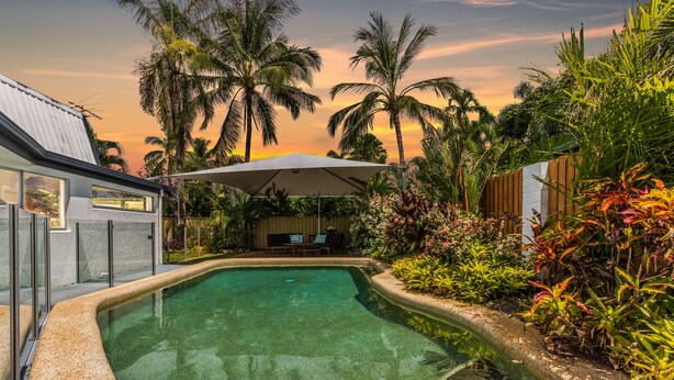 A swimming pool with a curved edge, surrounded by tropical plants and palm trees. - Tropical Beachside Home - Pool, Wifi (Holloways Beach)