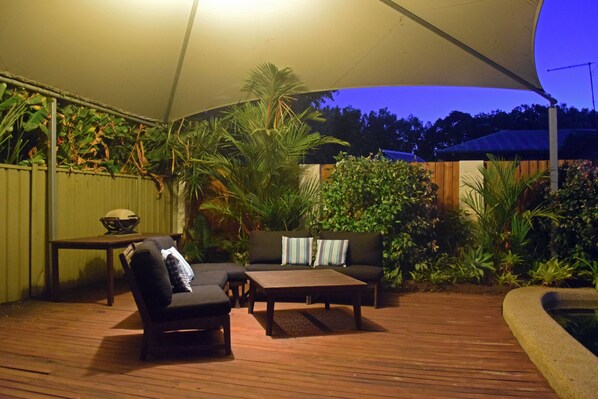 An outdoor patio with a wooden deck, a sofa, a chair, and a table. - Tropical Beachside Home - Pool, Wifi (Holloways Beach)