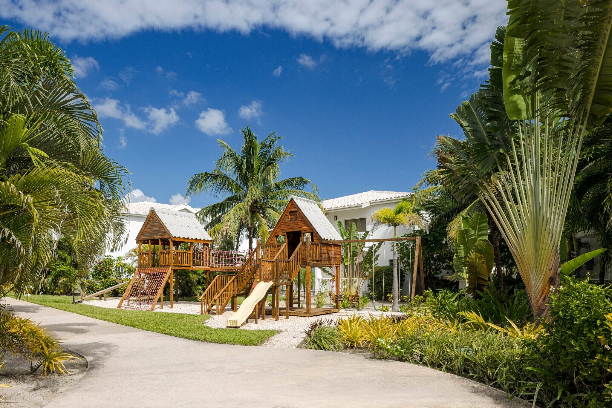 A resort with two wooden playhouses, a paved walkway, and tropical vegetation.