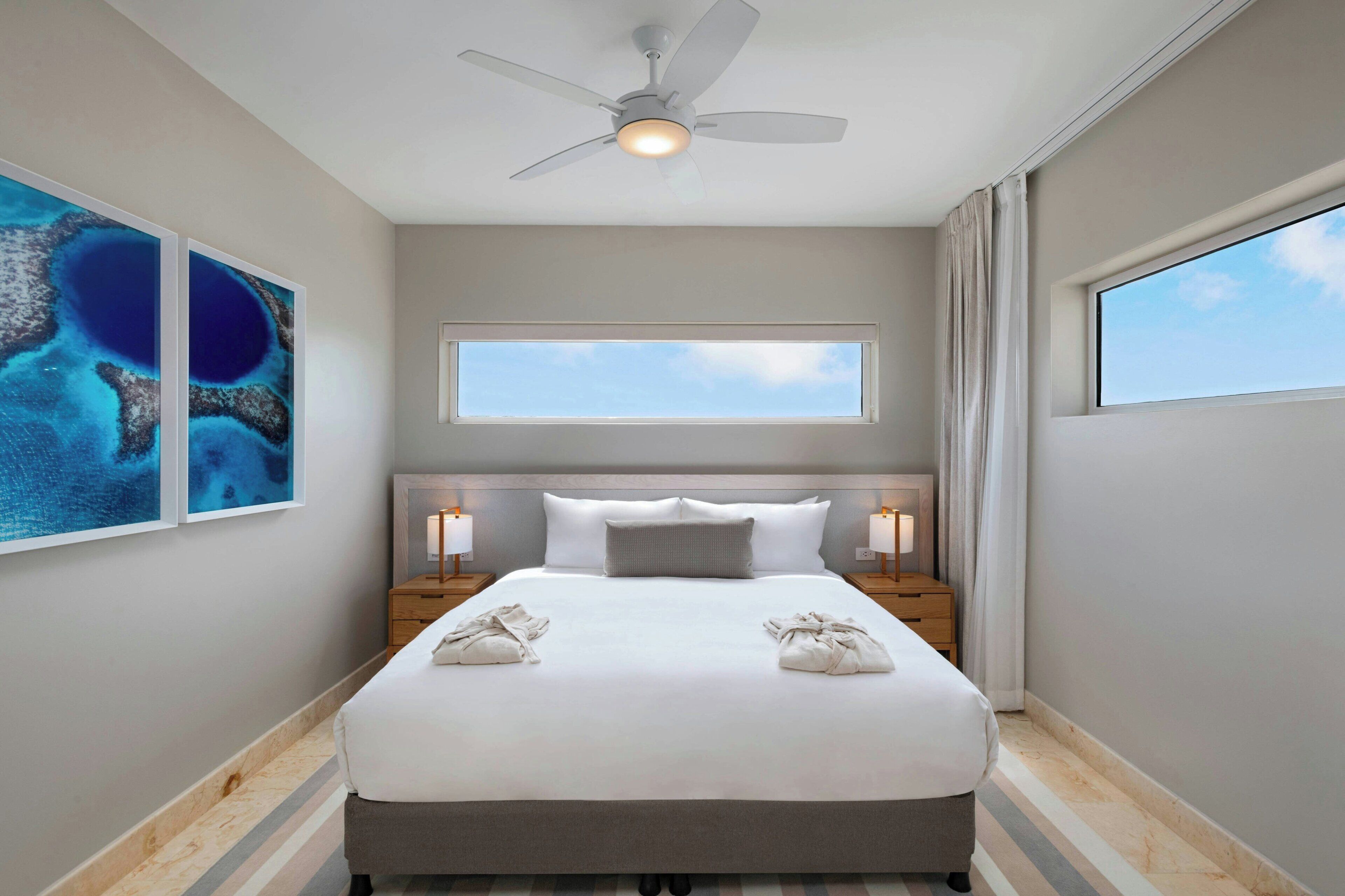 Hotelkamer met een bed, twee nachtkastjes, een plafondventilator, een raam en kunst aan de muur.