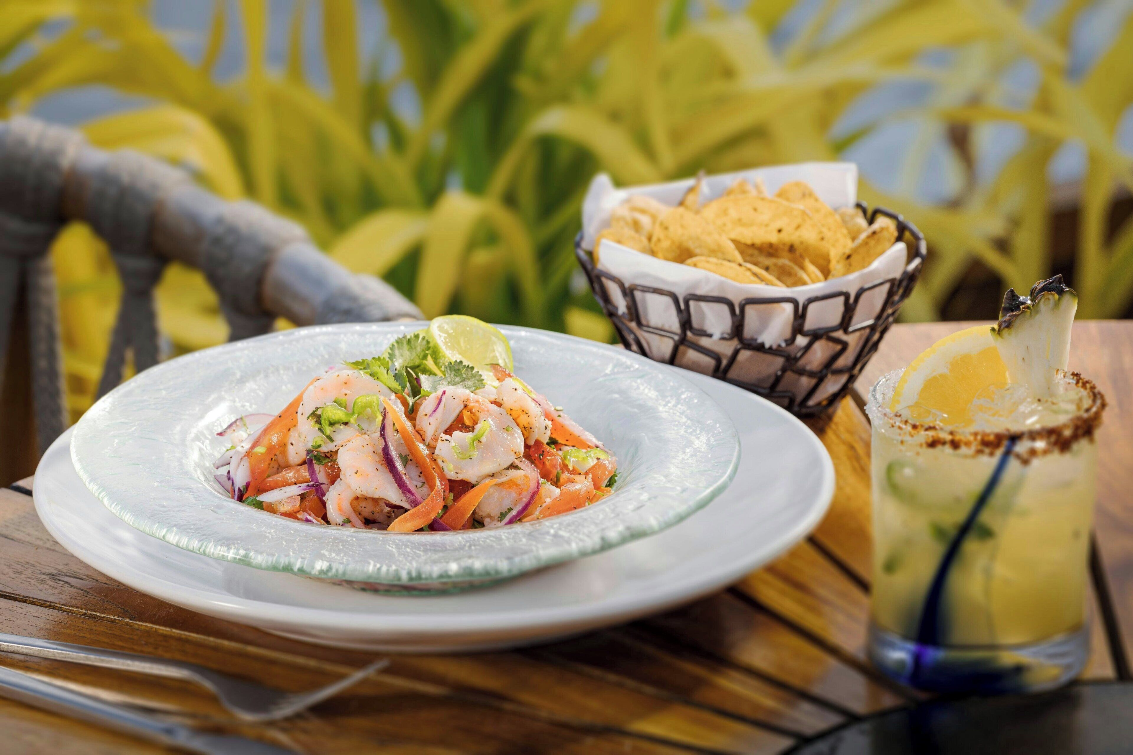 A plate of shrimp salad with a lime wedge, a basket of tortilla chips, and a margarita with a salted rim.