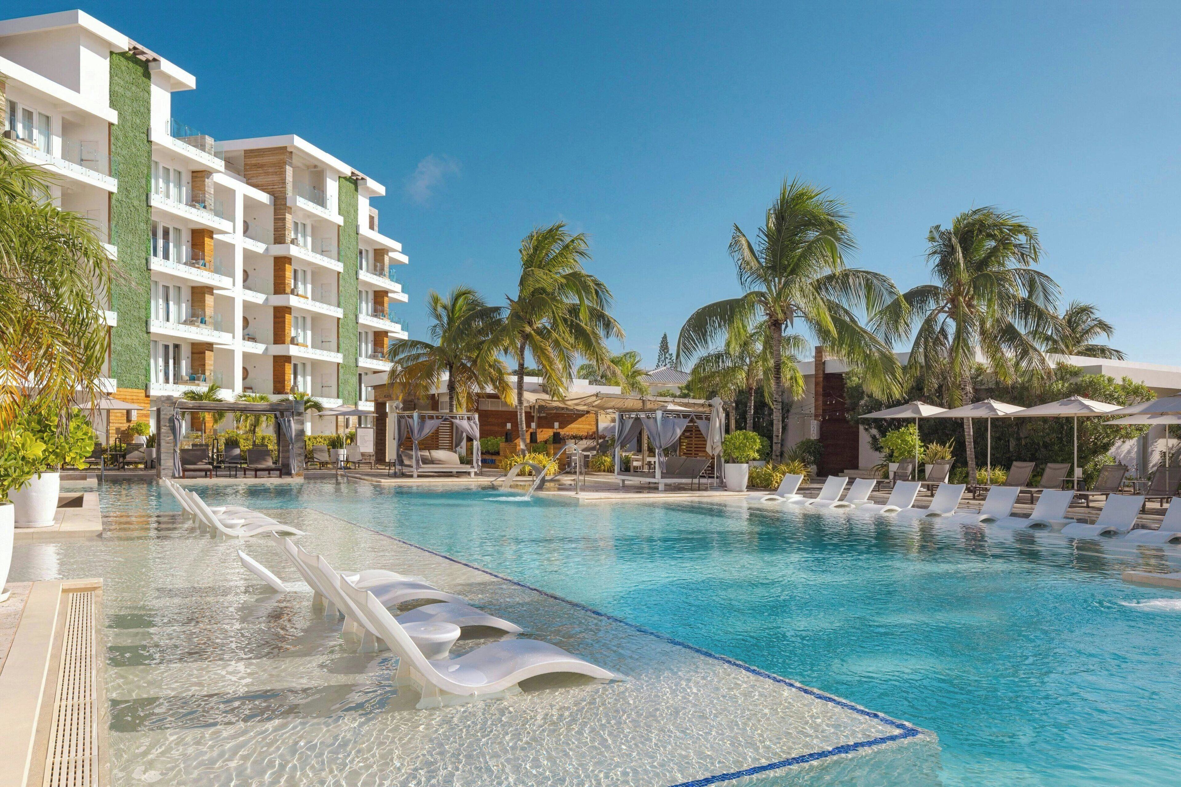 A resort pool with clear water, lounge chairs, and palm trees.