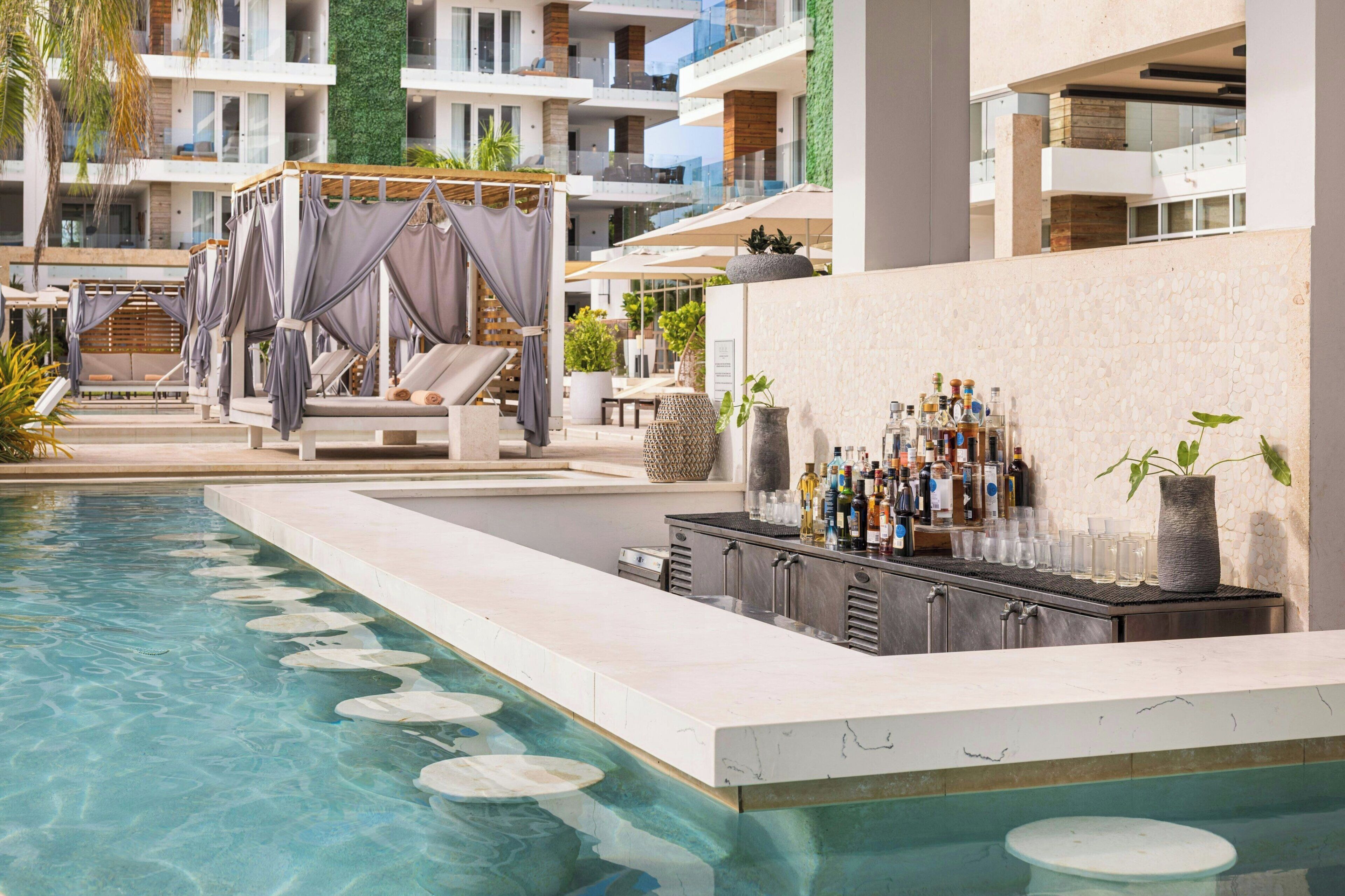 Zona de piscina con sillones reclinables, un bar y vista al edificio.