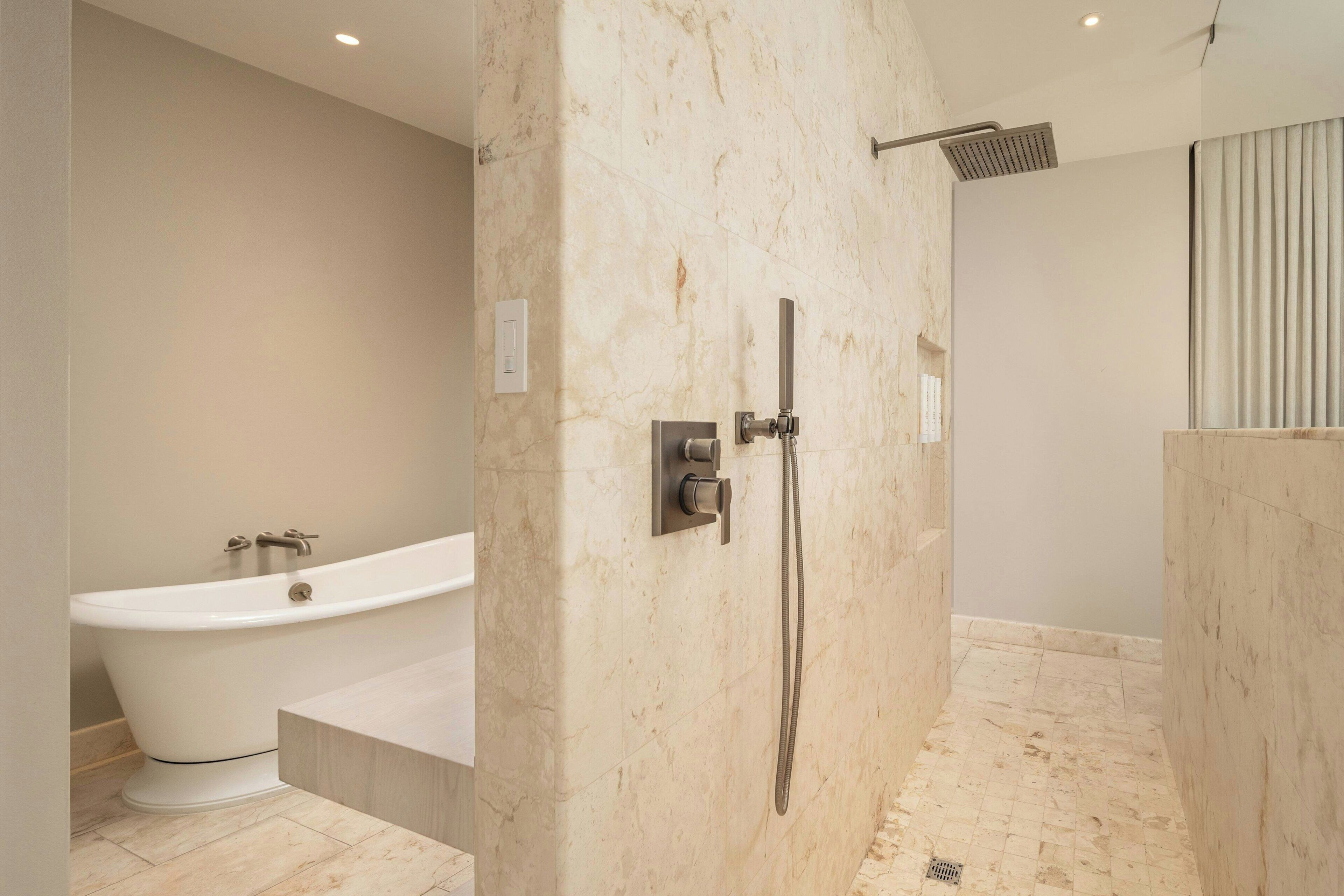 A modern bathroom with a freestanding bathtub, a walk-in shower, and a marble wall.