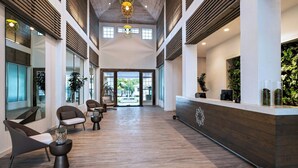 Un vestíbulo amplio con suelo de madera, asientos modernos y una recepción con plantas.