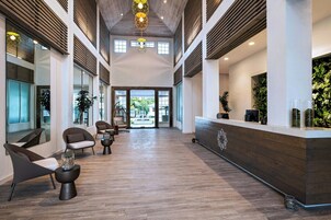 A spacious lobby with wooden flooring, modern seating, and a reception desk with greenery.