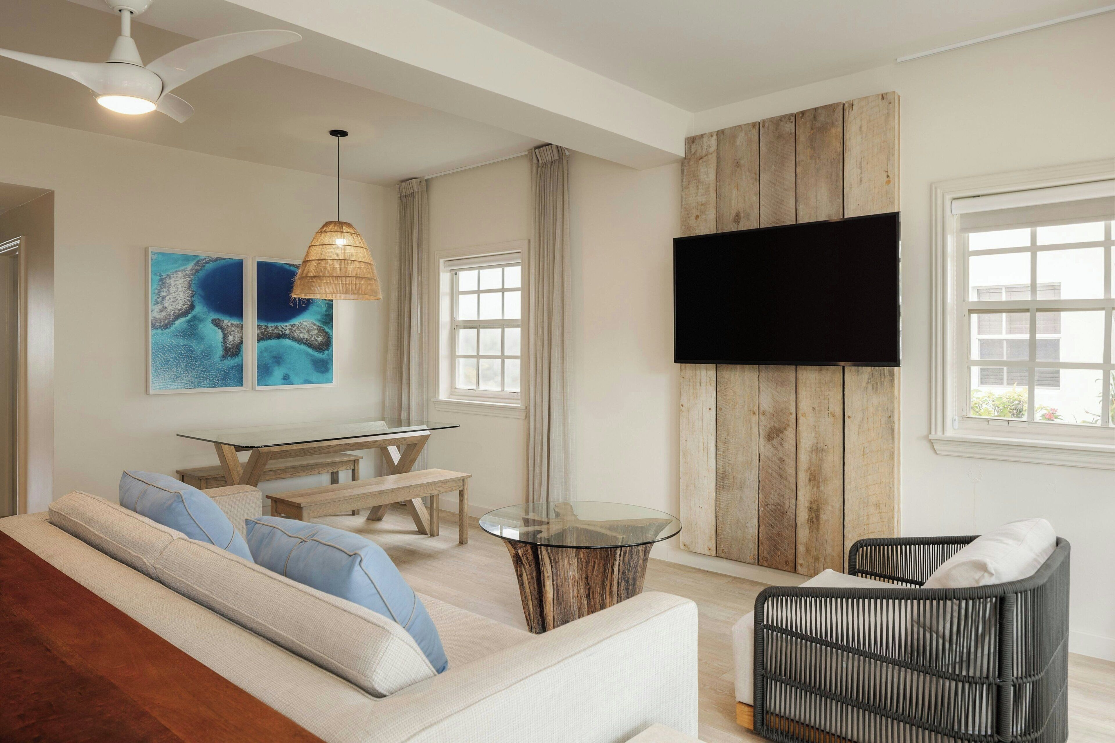 Un salon moderne comprenant un canapé, une table à manger, un téléviseur fixé à un mur en bois et une grande fenêtre.