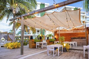 Een terras buiten met houten tafels en stoelen, lichtslinger en een houten pergola.