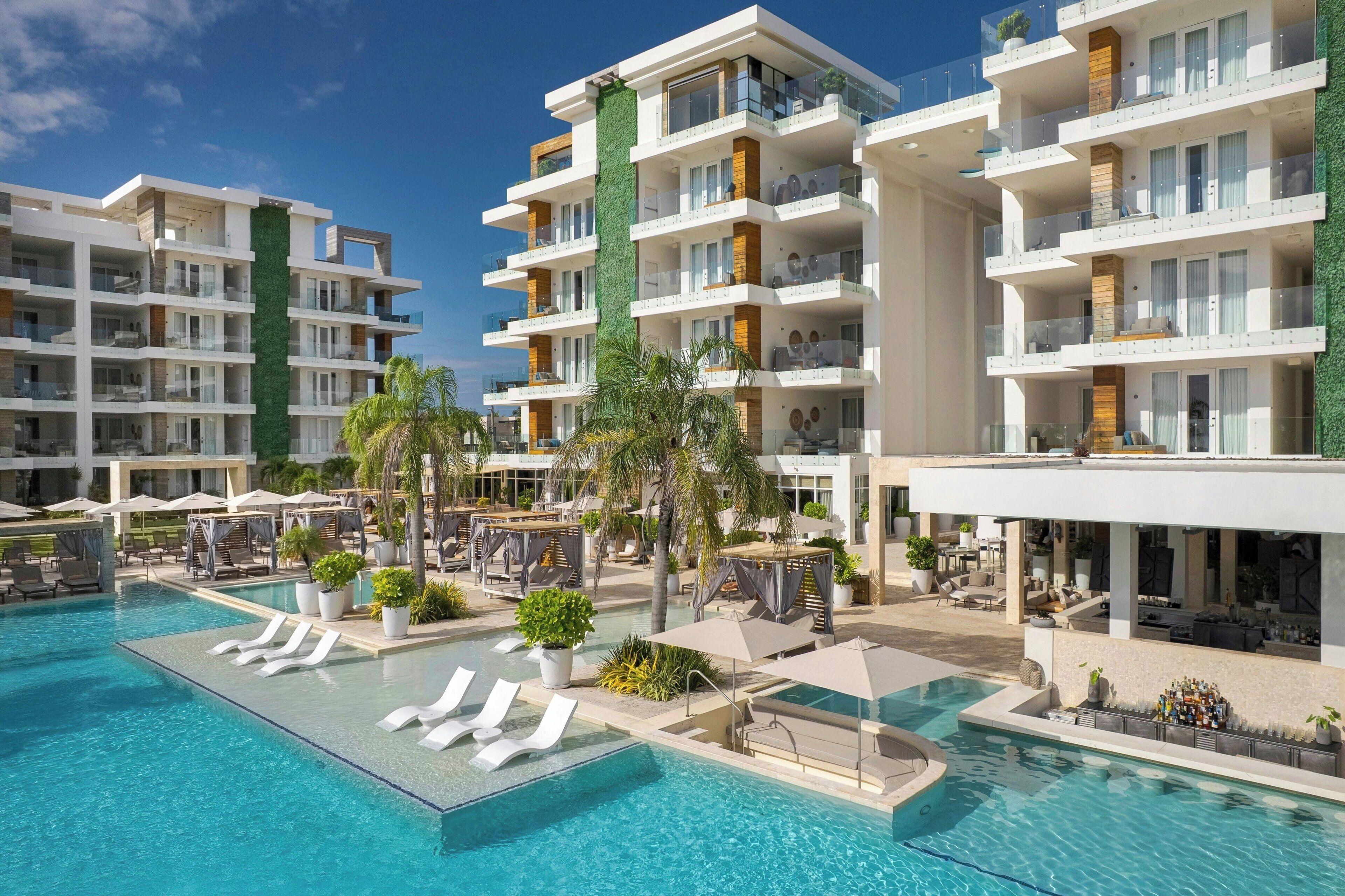 Un hotel moderno con varios balcones, piscina y zonas de estar al aire libre.