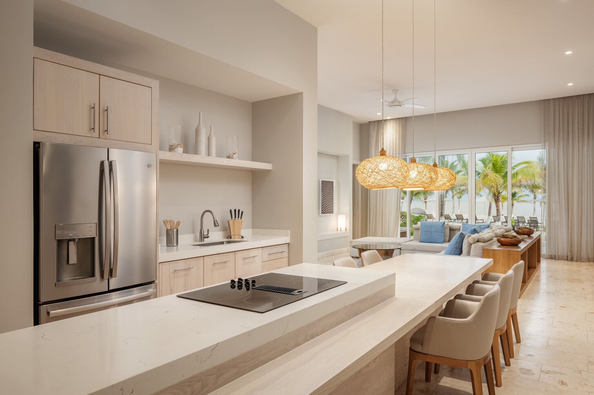Una cocina moderna con una isla grande, electrodomésticos de acero inoxidable y vistas a un balcón con mobiliario exterior.