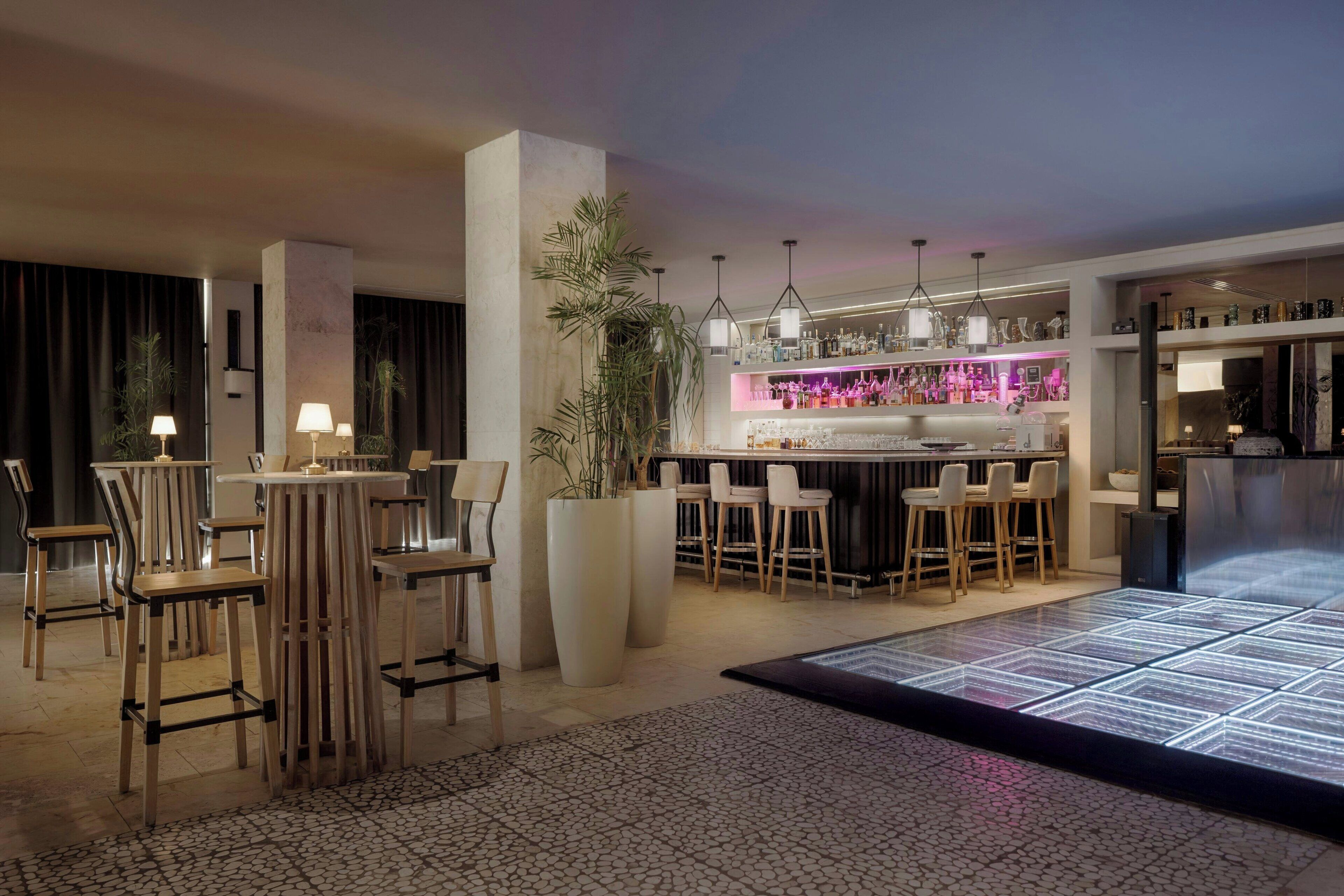 A modern bar area with stools, a bar counter, and a variety of bottles.