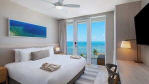 Un cuarto de hotel con una cama grande, un ventilador de techo, un televisor, un escritorio y vista al océano.