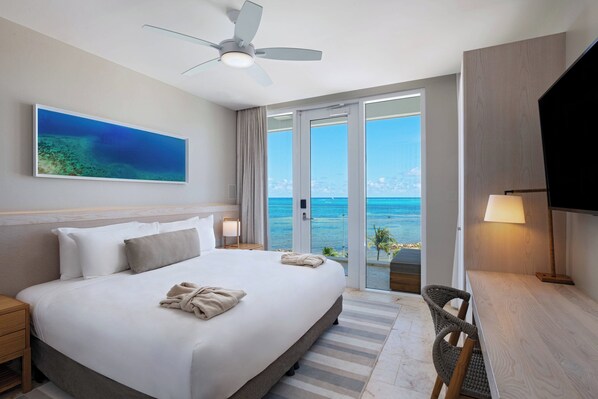 A hotel room with a large bed, a ceiling fan, a TV, a desk, and a view of the ocean. - Alaia Belize, Autograph Collection  (San Pedro)