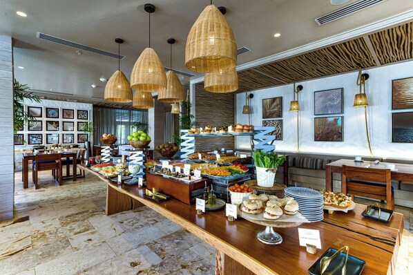 A buffet setup with various food items and a seating area with tables and chairs. - Alaia Belize, Autograph Collection  (San Pedro)