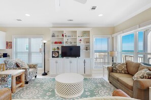 A living room with a TV, white cabinets, and a view of the ocean.
