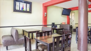 Un restaurante con mesas tipo cabina y mesas comunes, un televisor montado en la pared y un pilar rojo.