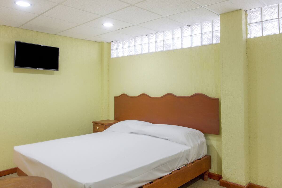 Una cama individual con cabecera de madera en una habitación con techo de baldosas y ventana con cristal satinado.