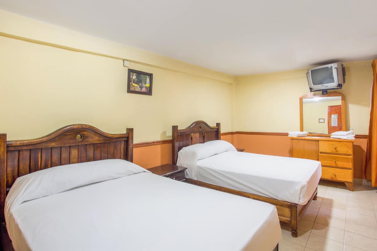 A hotel room with two single beds, a wooden dresser, a television on a stand, and a framed picture on the wall.