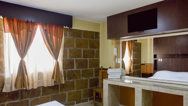 Una habitación de hotel con cama, tocador en el baño, espejo y pared de ladrillo.