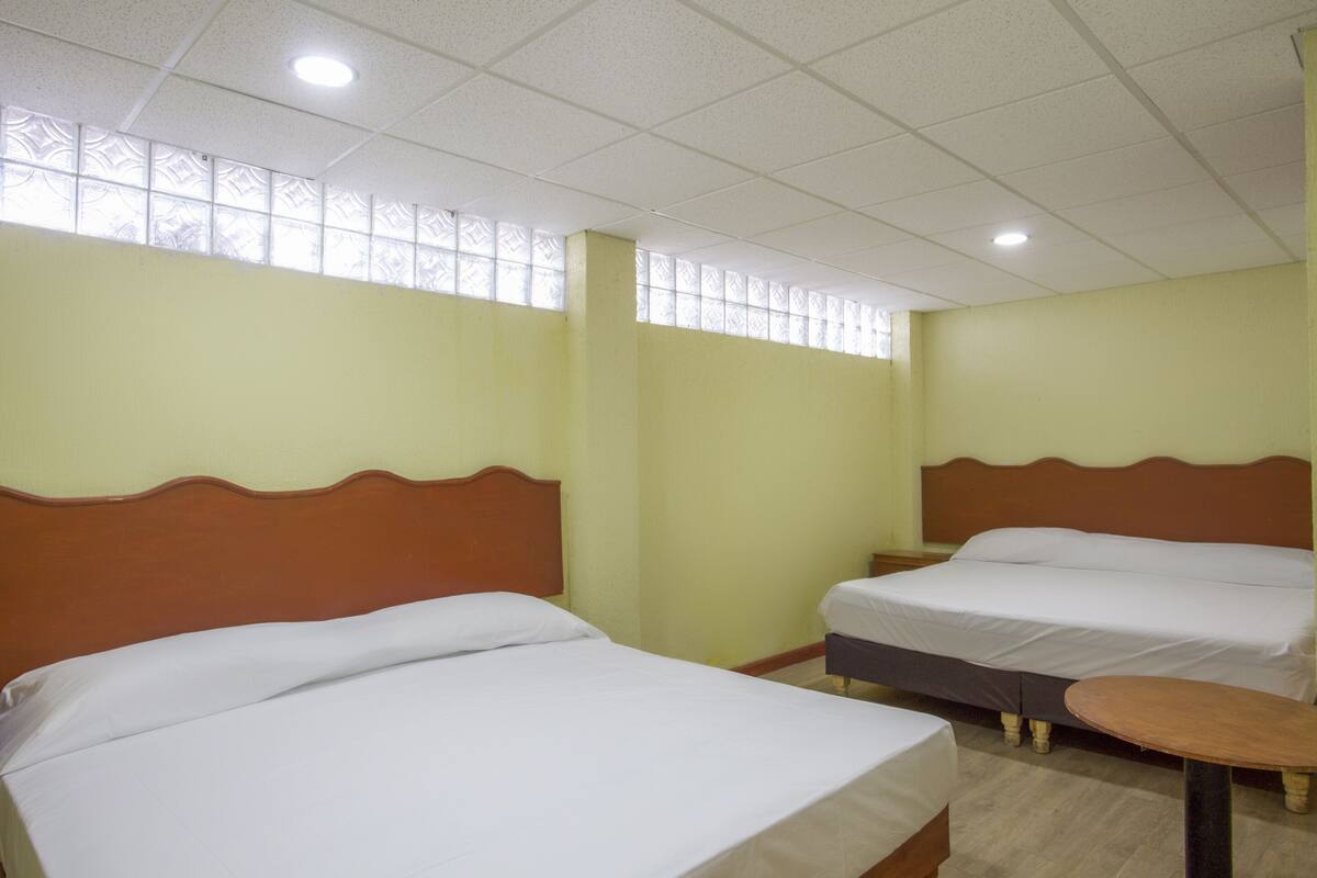 Habitación de hotel con dos camas, una mesita y un ventanal con diseño decorativo.