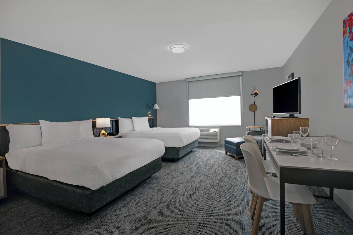 Una habitación de hotel moderna con dos camas, un escritorio, un televisor y un ventanal grande.