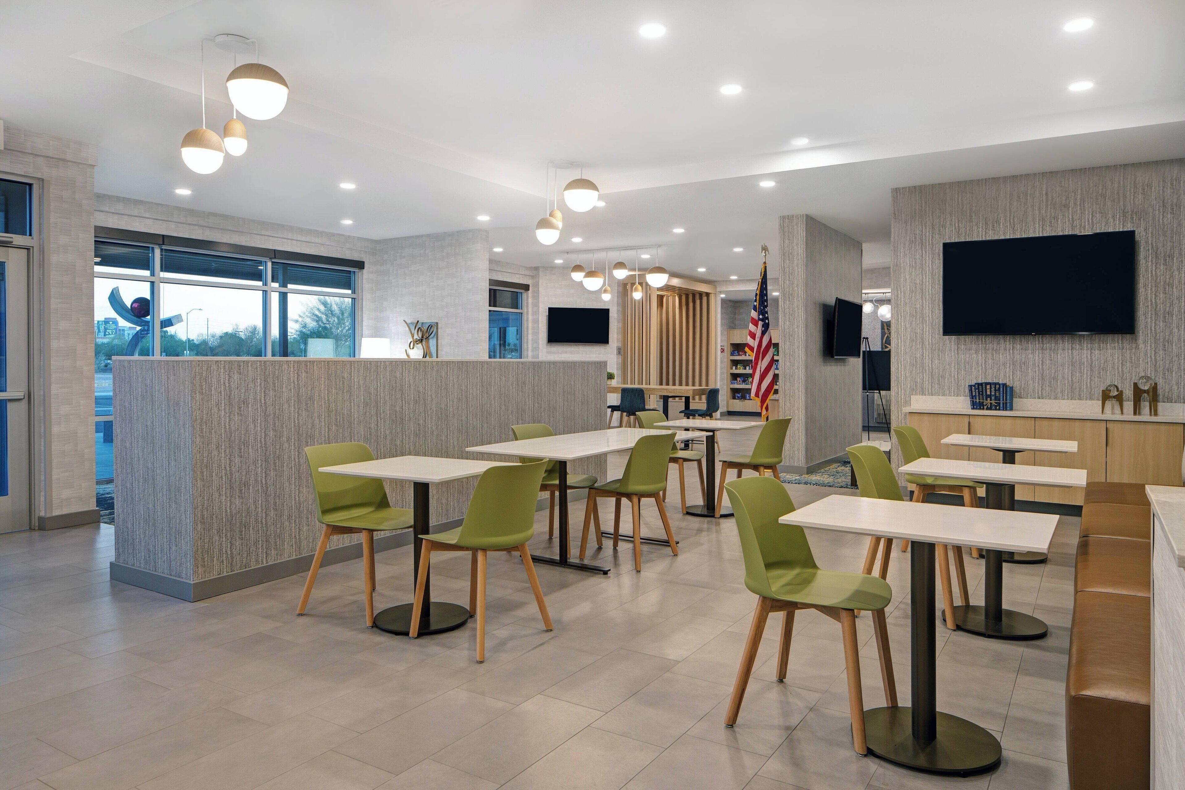 A modern dining area with tables and chairs, a reception desk, and a television screen.