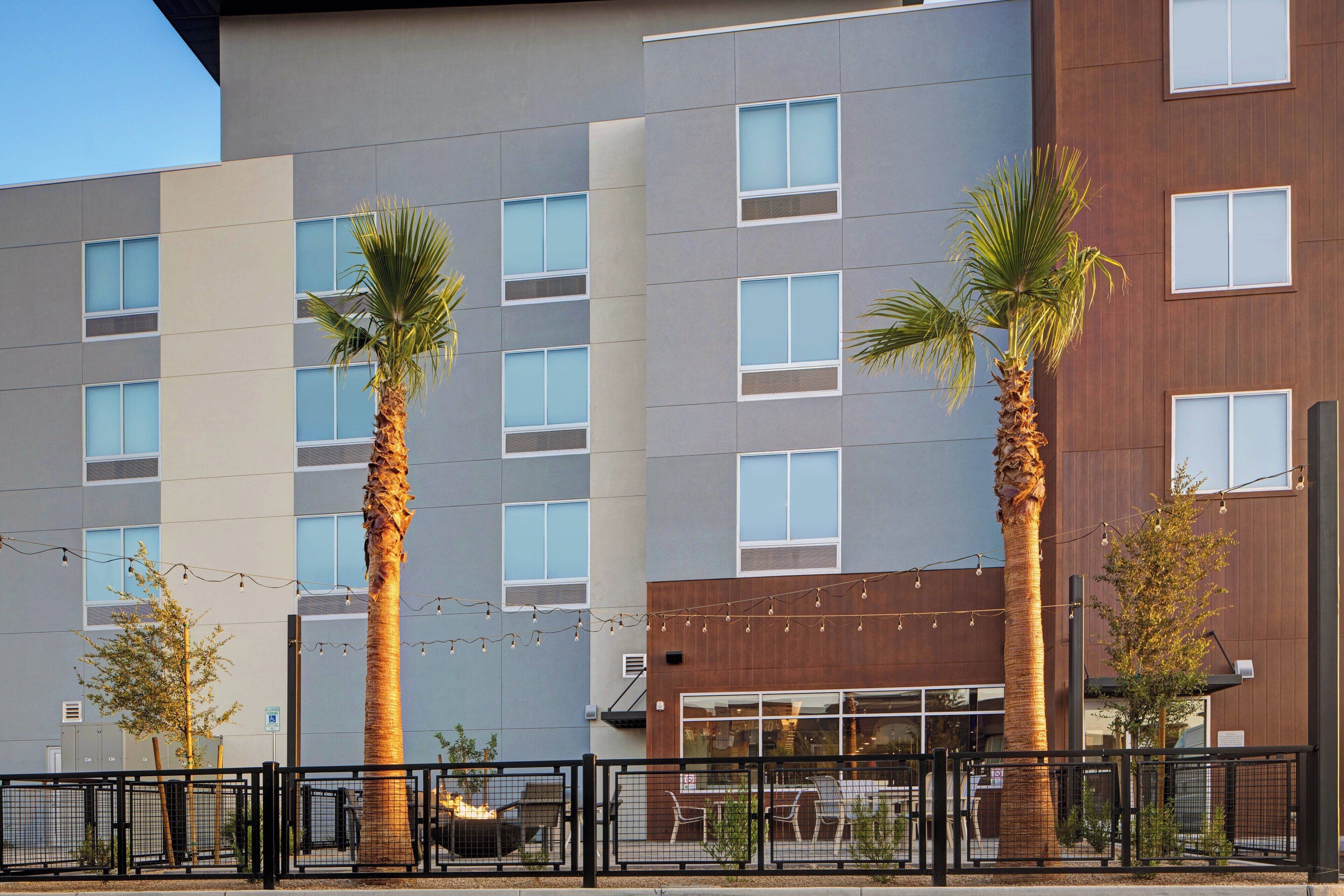 A modern building with multiple windows and palm trees in front.
