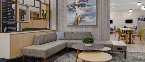 A modern hotel lobby with a sectional sofa, round tables, and a large abstract painting on the wall.