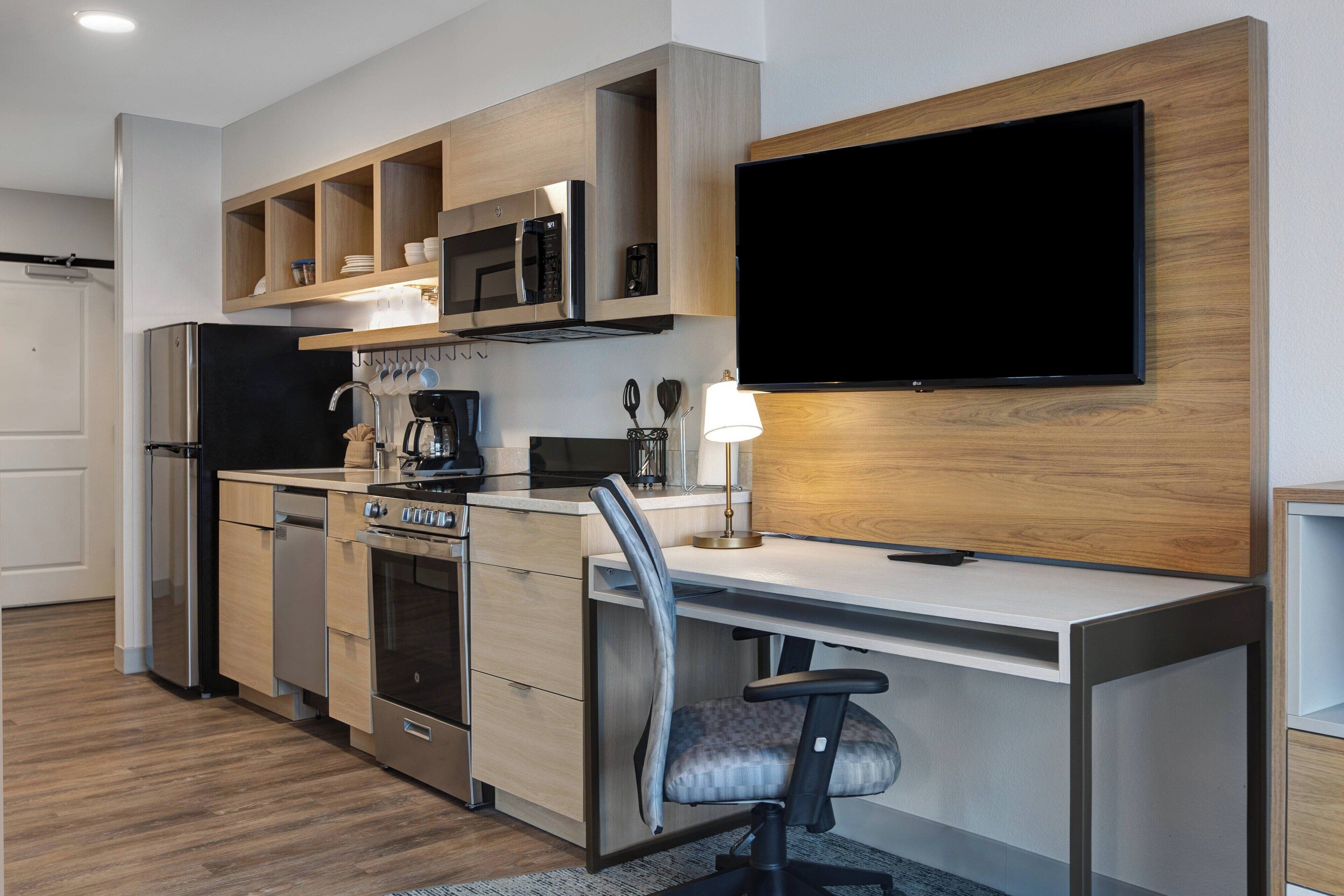 A modern kitchen with built-in appliances, a flat-screen TV, and a workspace with a chair.