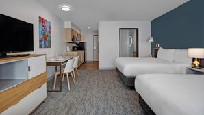 Habitación de hotel con televisor, escritorio con sillas, cama y kitchenette.