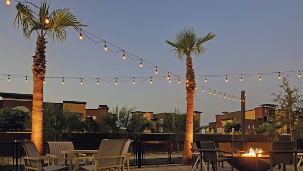 Un patio al aire libre con luces colgantes, palmeras y mobiliario exterior.
