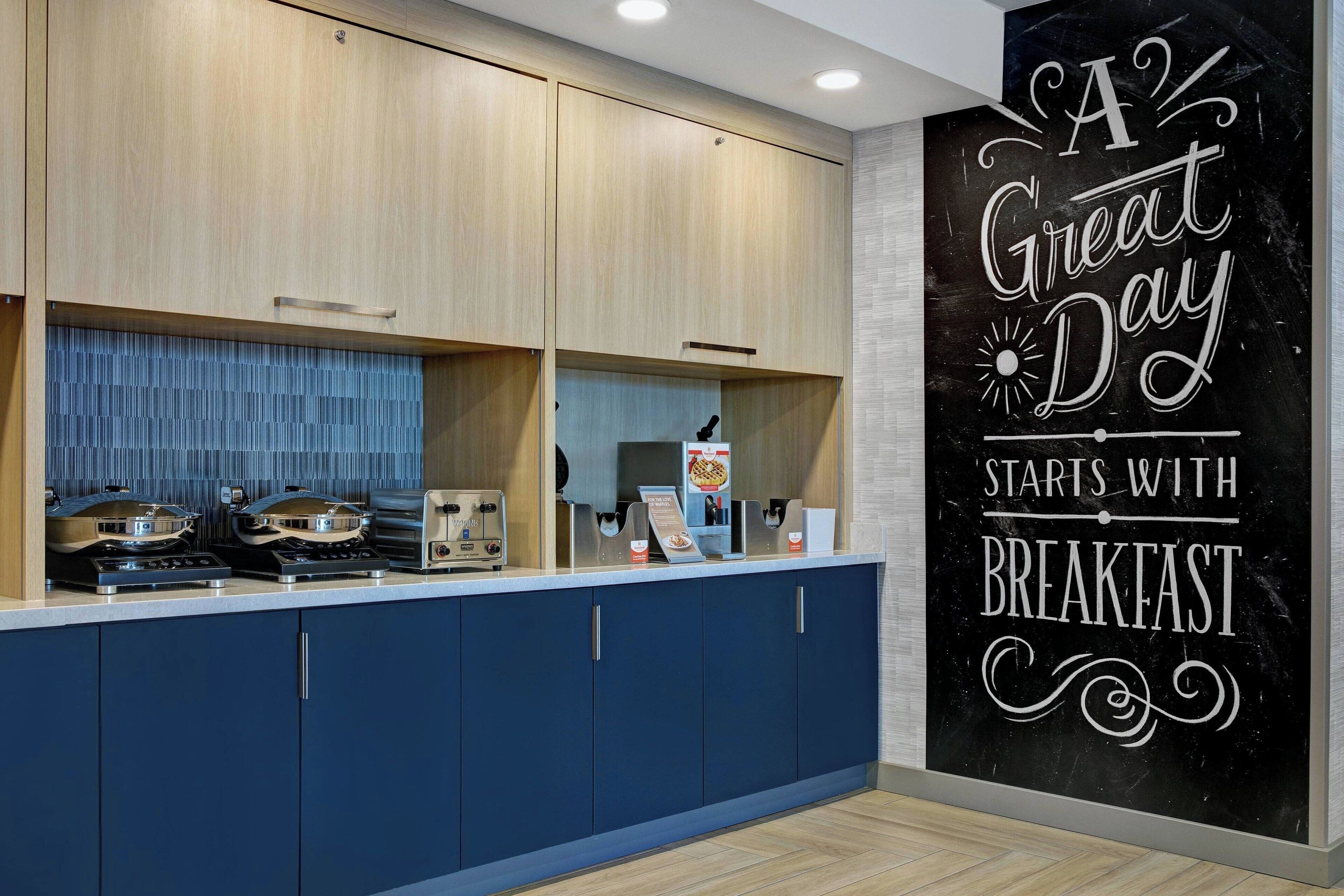 A modern kitchen with wooden cabinets, a blue countertop, and a chalkboard wall with a motivational message.